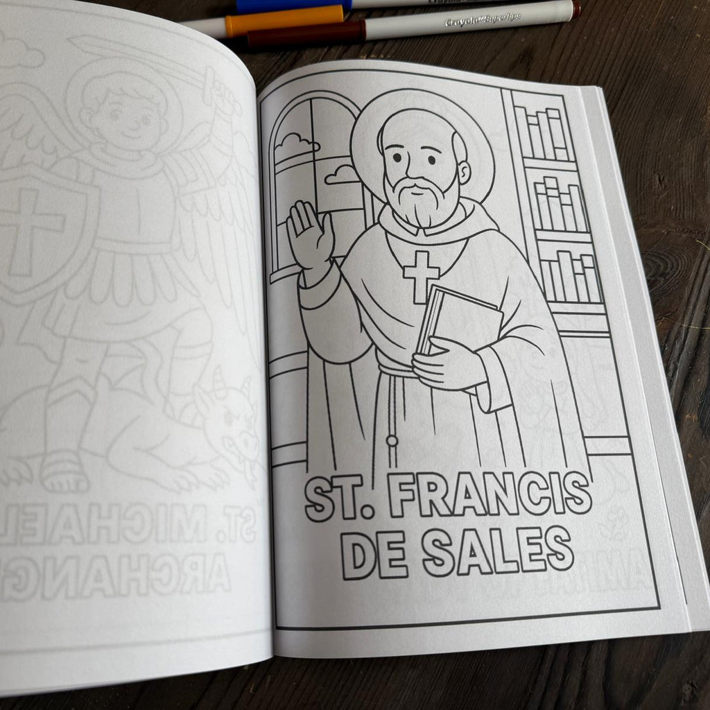 Coloring book open to a page with a black and white illustration of St. Francis de Sales, with markers on a wooden surface.